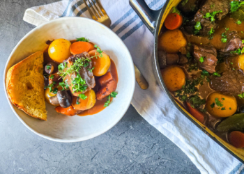 Holiday recipe Beef Bourguignon in a large pot and also in a smaller bowl, with linen towel underneath and a gold fork.
