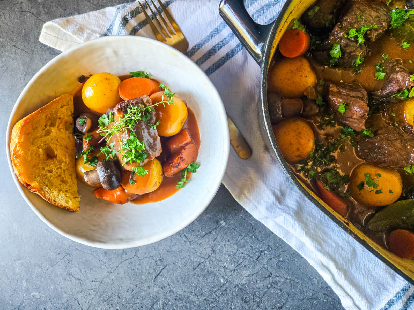 Holiday recipe Beef Bourguignon in a large pot and also in a smaller bowl, with linen towel underneath and a gold fork.