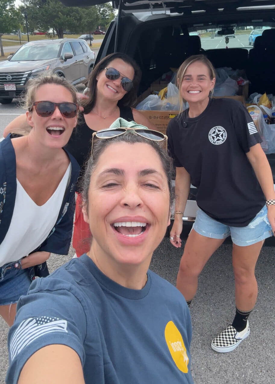 Ashlee Sullivan volunteers with Stronghold Food Pantry, which supports military families facing food insecurity. She stands with three other friends in front of a car trunk filled with groceries to distribute.