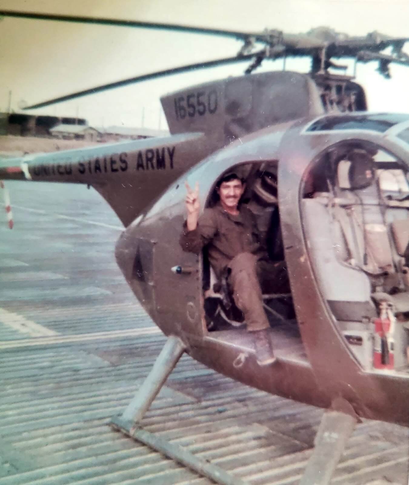 Army soldier Abel Garcia smiles and gives a peace sign with his fingers in a helicopter during the Vietnam War era.