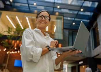 Business woman smiles as she holds a laptop in her hands.