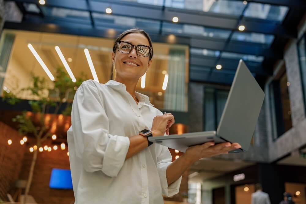 Business woman smiles as she holds a laptop in her hands.