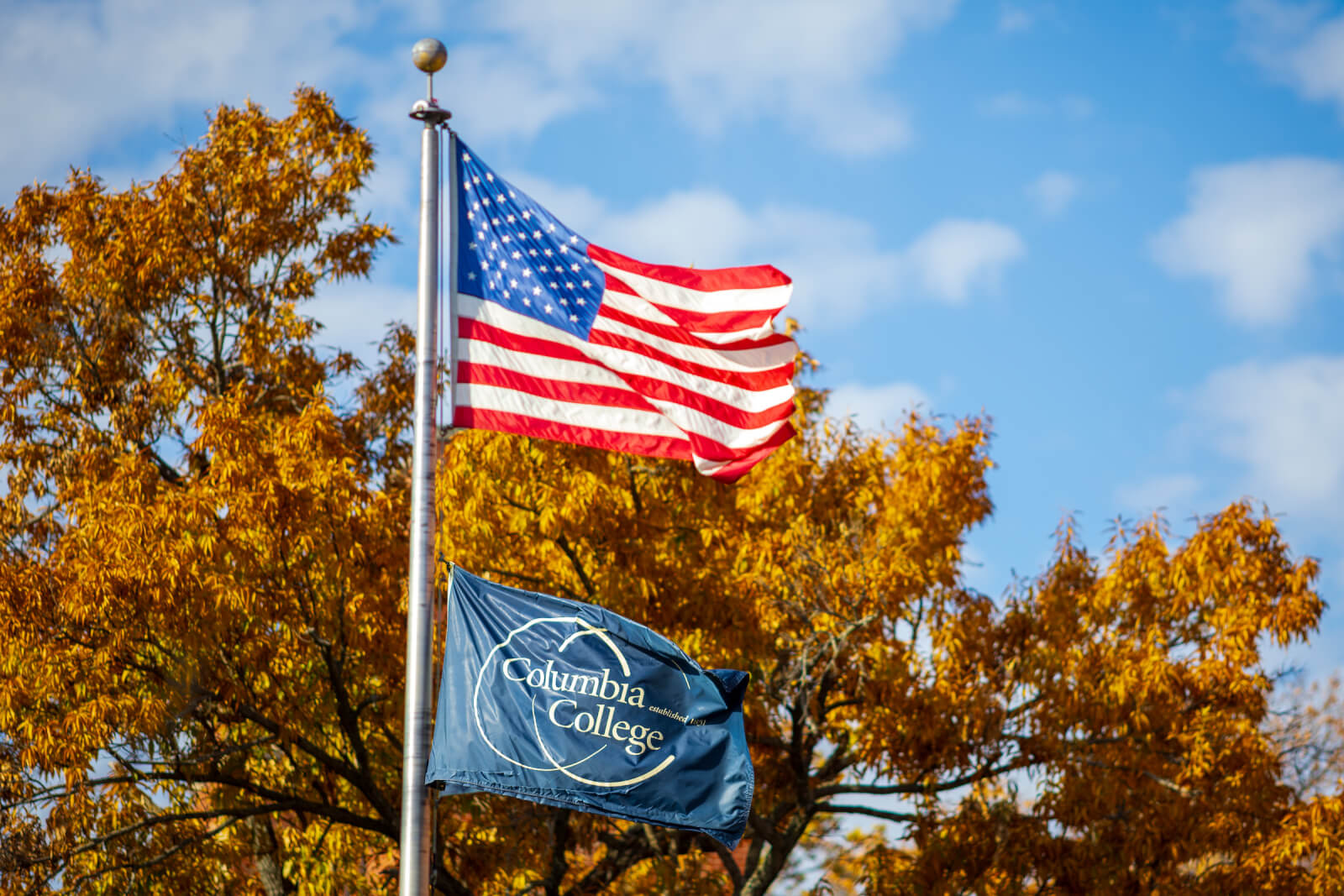 American flag flies on flagpole with a Columbia College flag beneath it.