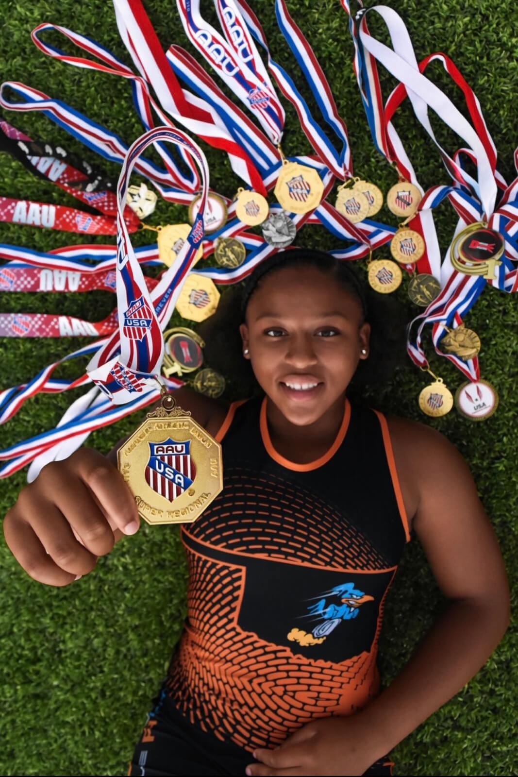 Military kid Khloe Pollard lies on the grass surrounded by her numerous medals, holding one up to the camera as she smiles.